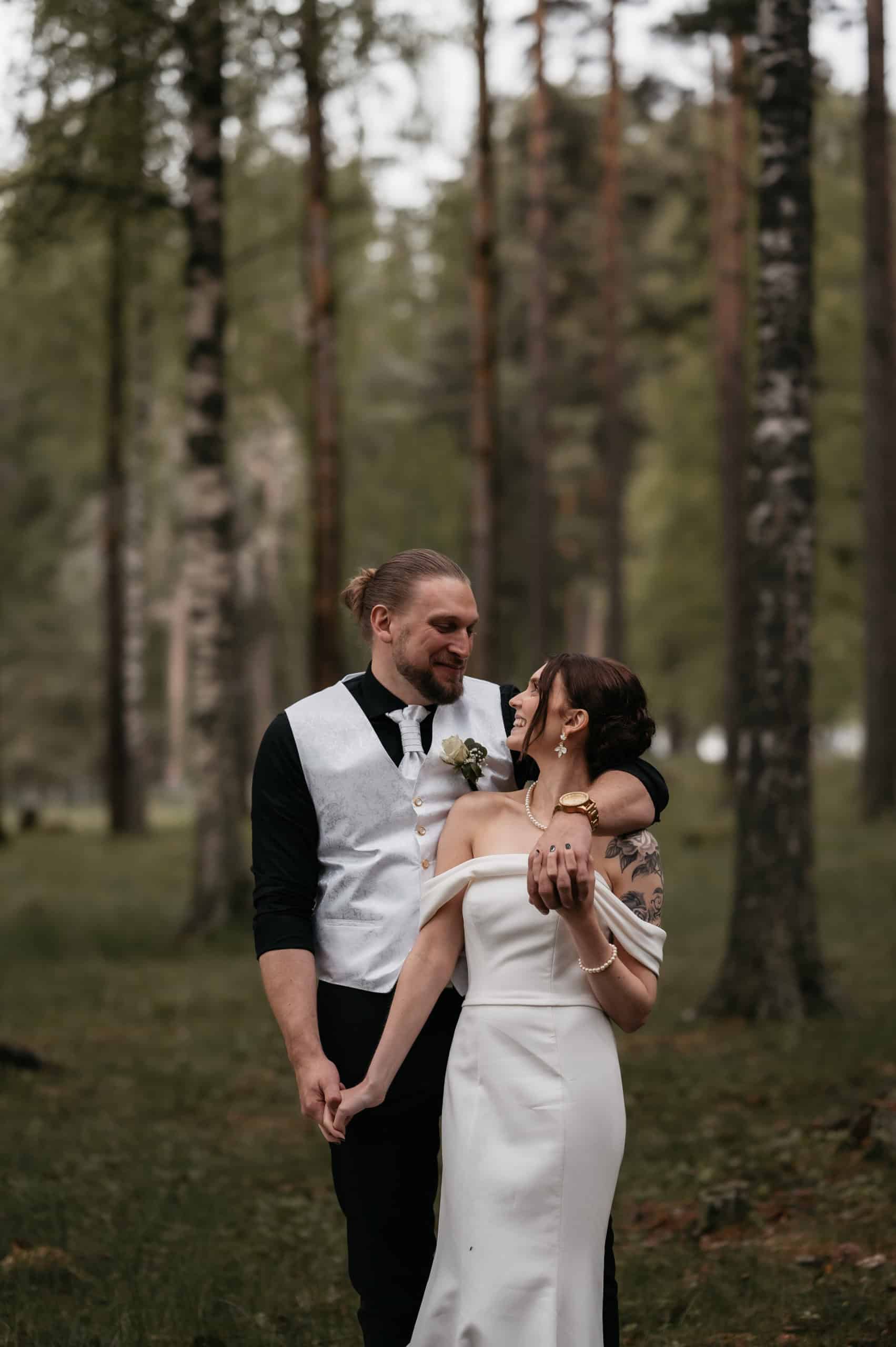 Nydelig bryllupsfoto i skog med brudepar som holder hender og ser på hverandre.