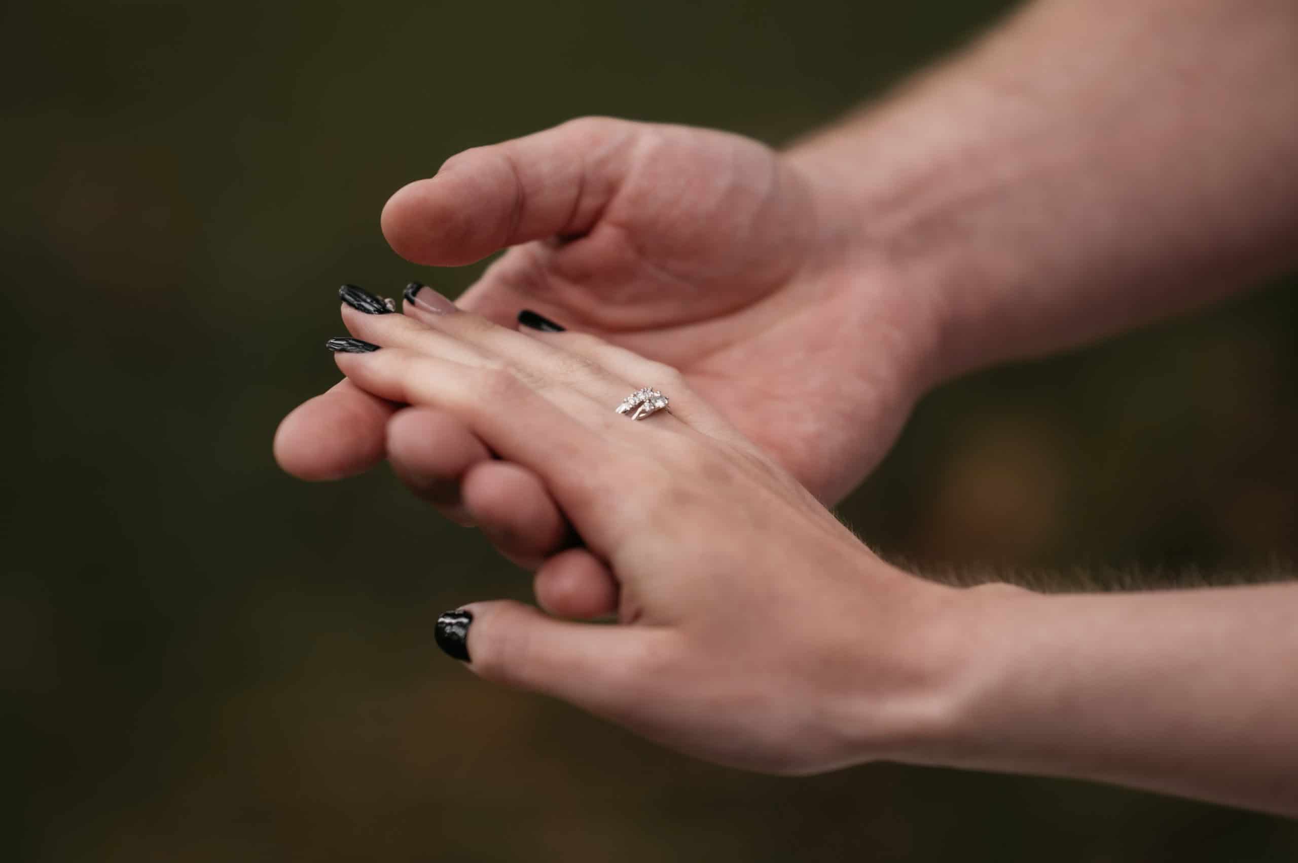 Nærbilde av hender med forlovelsesring under regnfullt maibryllup.