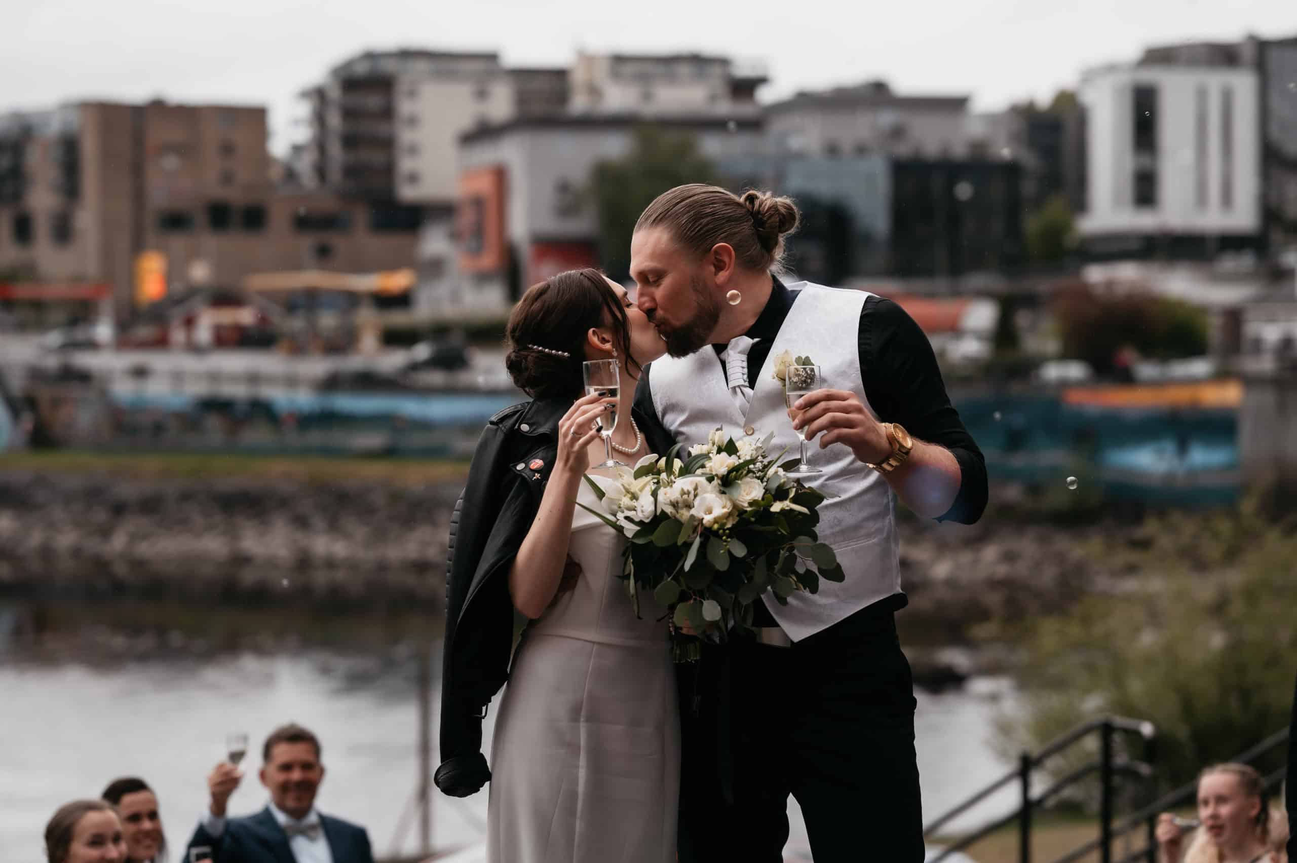 Bryllupspar kysser ved elvepromenade i Hønefoss under regnfull maibryllup.