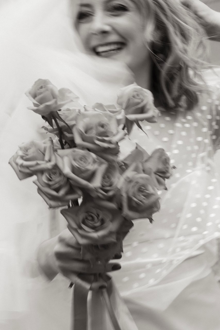 Kvinne med blomstertopp holder en stor bukett med rosa roser.