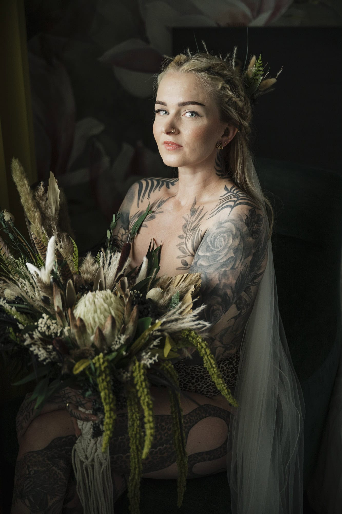 Kvinne med tatoveringer holder en stor blomsterbukett i studio.