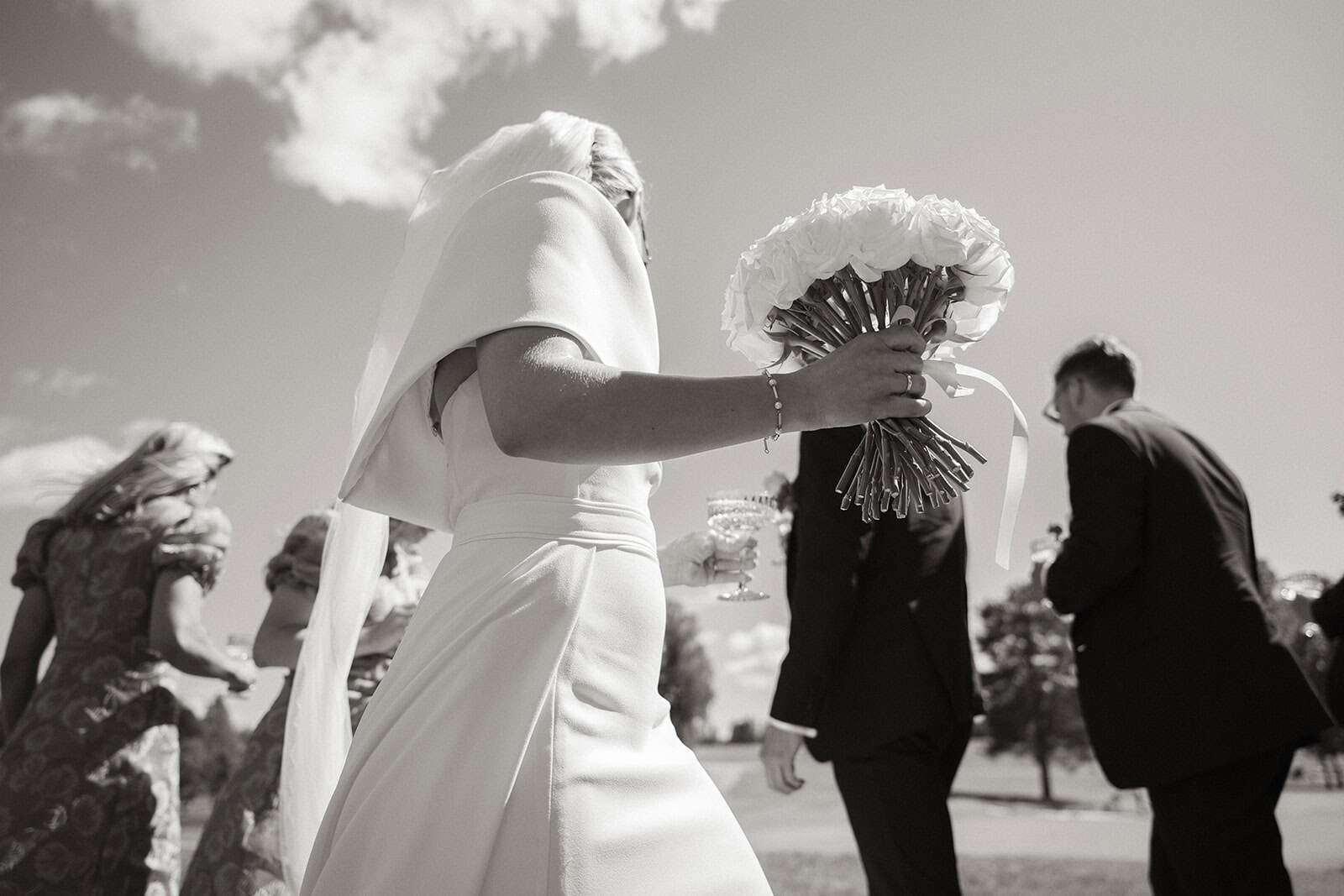 Brudepike med blomsterbukett under utendørs bryllup i solskinn.