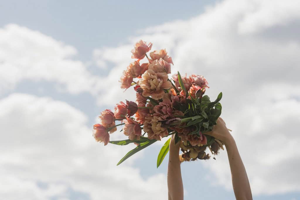 Person holder blomster mot skyen i bakgrunnen.