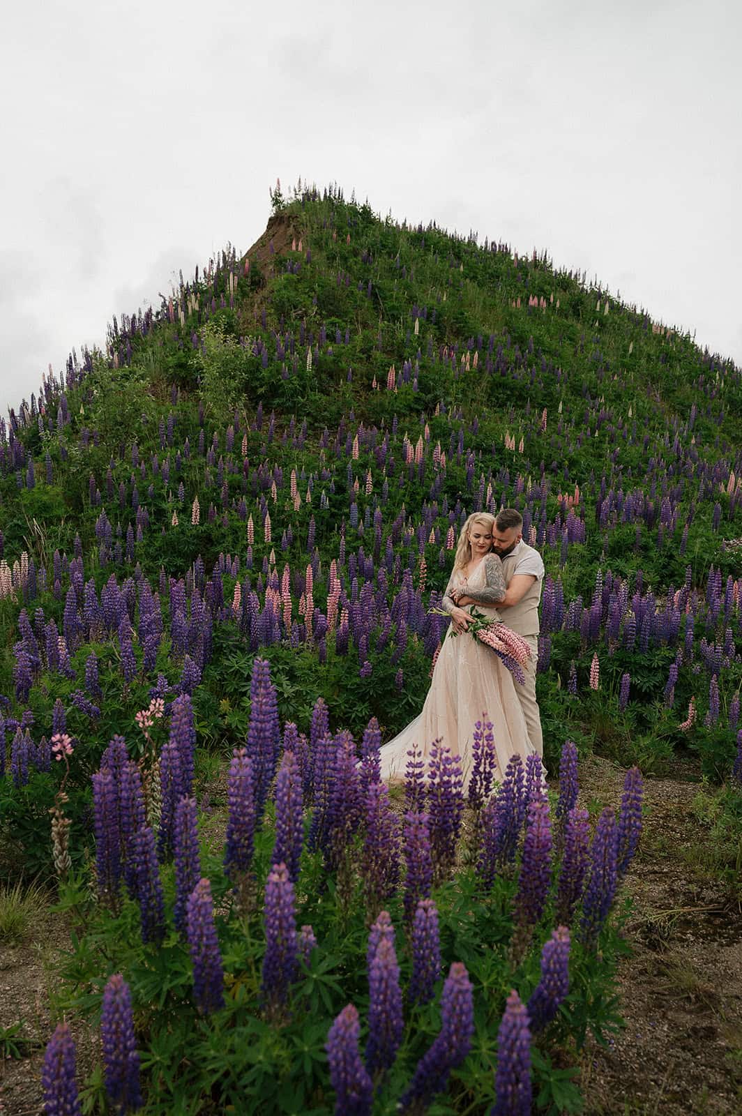 Bryllupsfoto med par i blomsterhage foran fjell med lavendel.