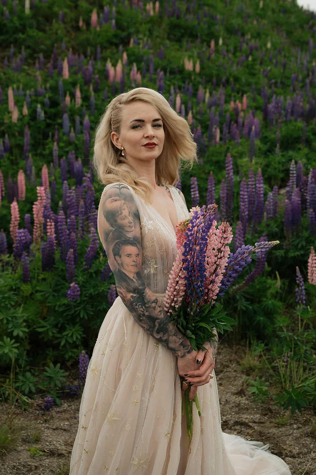 Kvinne med blond hår og tatoveringer i blomsterfelt med lupiner.