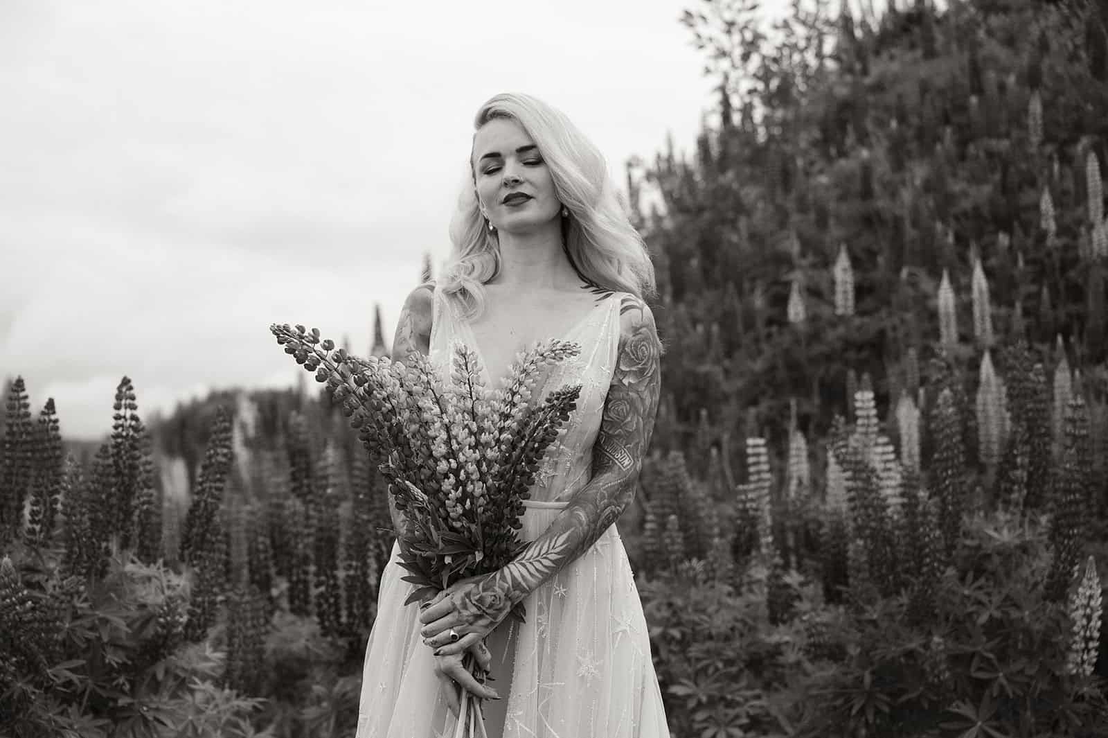 Kvinne med blondt hår holder en blomsterbukett i en blomstereng.