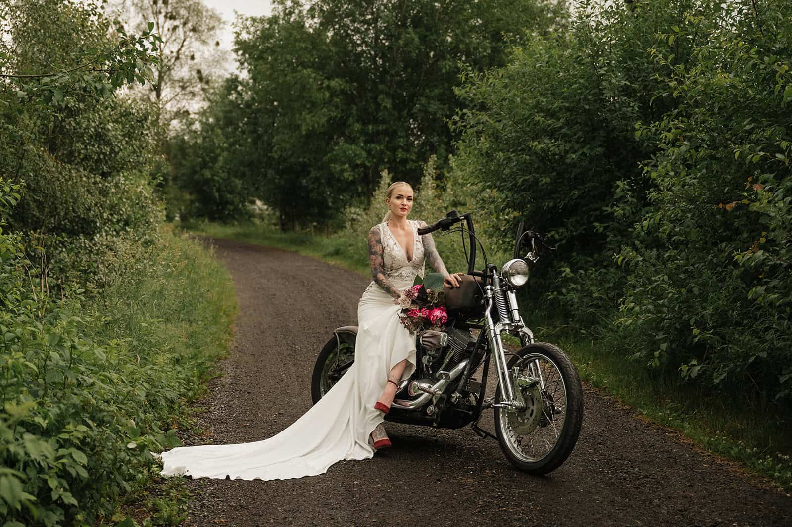 Brudepike på motorsykkel i grønt landskap med skog.