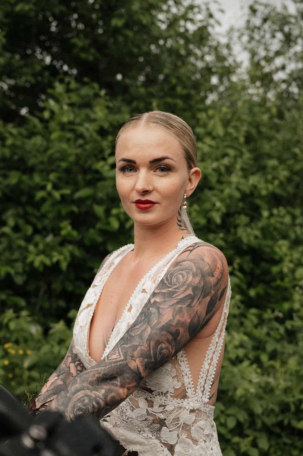 Kvinne med tatoveringer i en grønn park, iført hvit bluse.