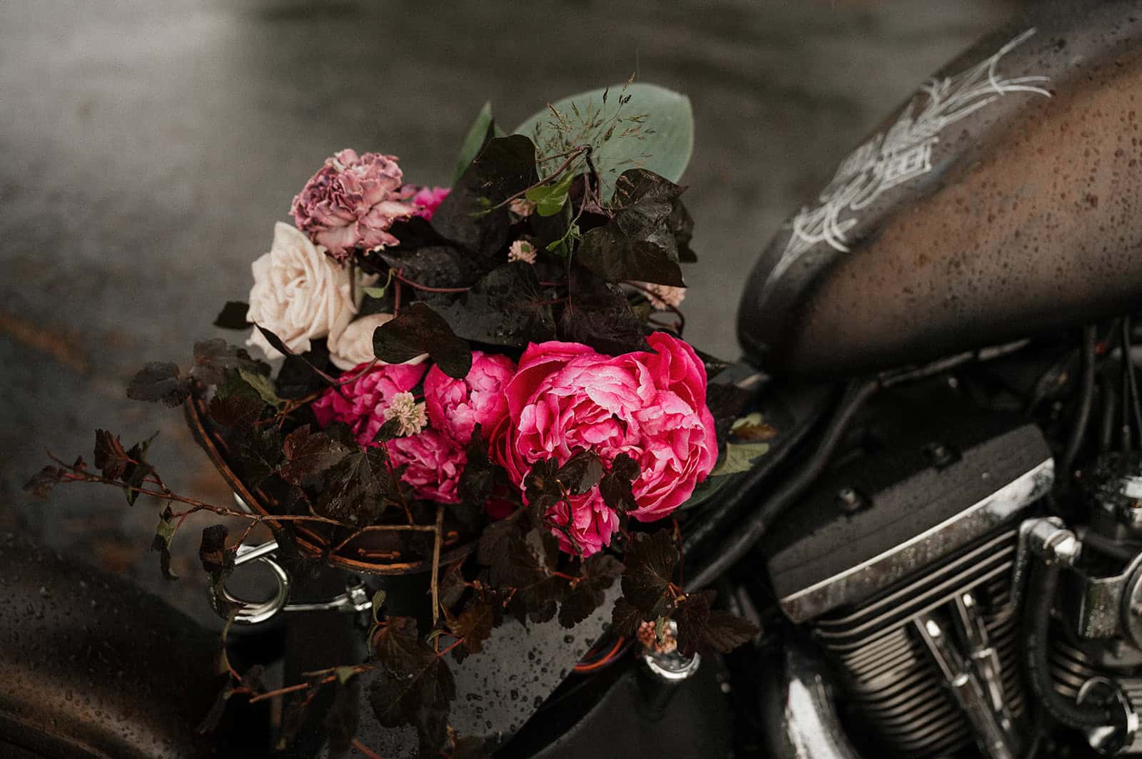 Blomster på motorsykkel med svart tank og motor, regnfulle forhold.