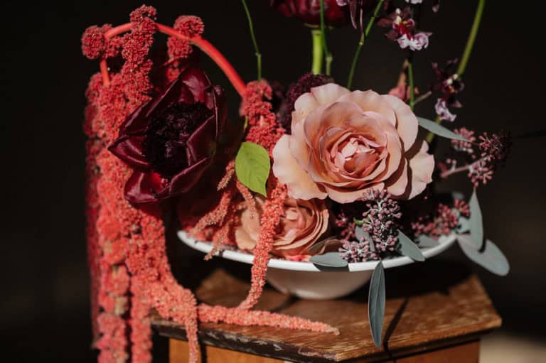 Elegant blomsterarrangement med roser og mørke blomster i en skål.