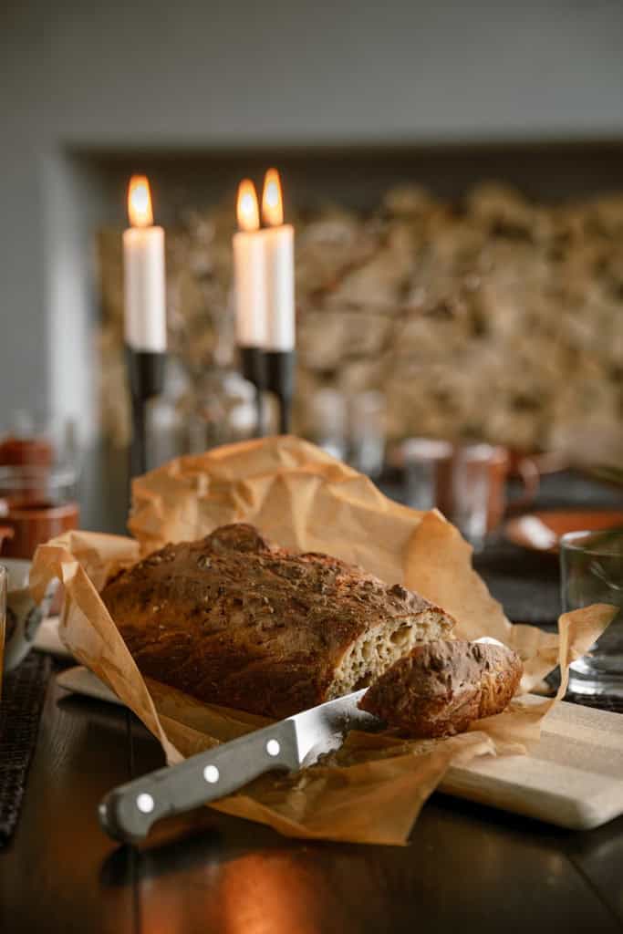 Nystekt brød og smør på et bord med levende lys i bakgrunnen.