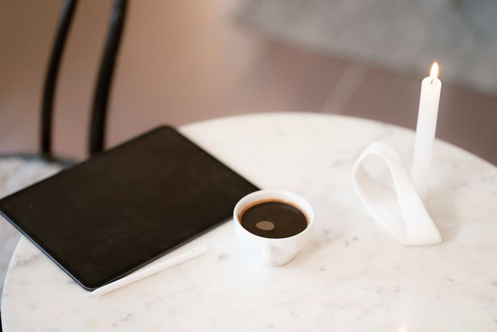 Kaffe, notatbok og lys på bord i koselig kafé.