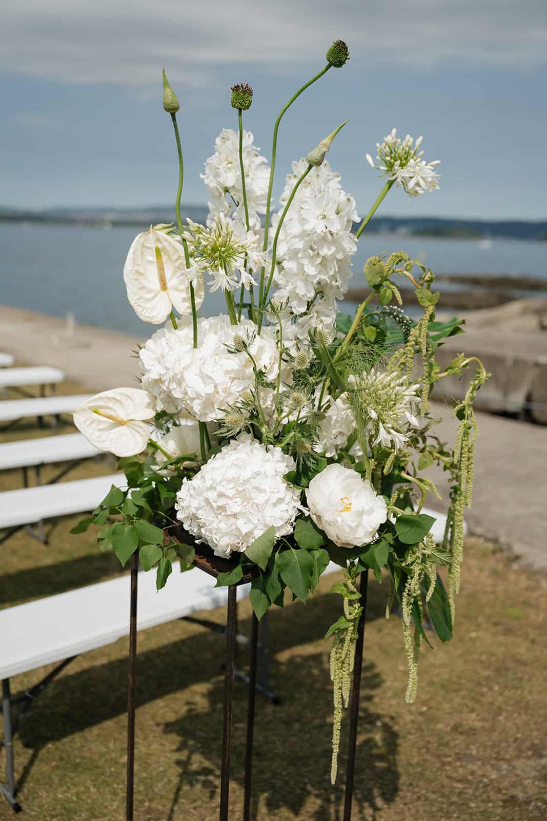 Elegant hvit blomsterarrangement med sjøutsikt i bakgrunnen.
