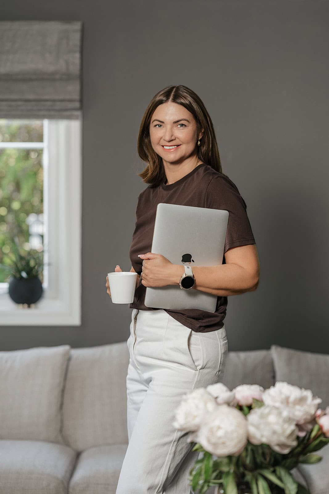 Kvinne smiler med laptop og kopp i stue, hjemmekontor, arbeid hjemmefra.